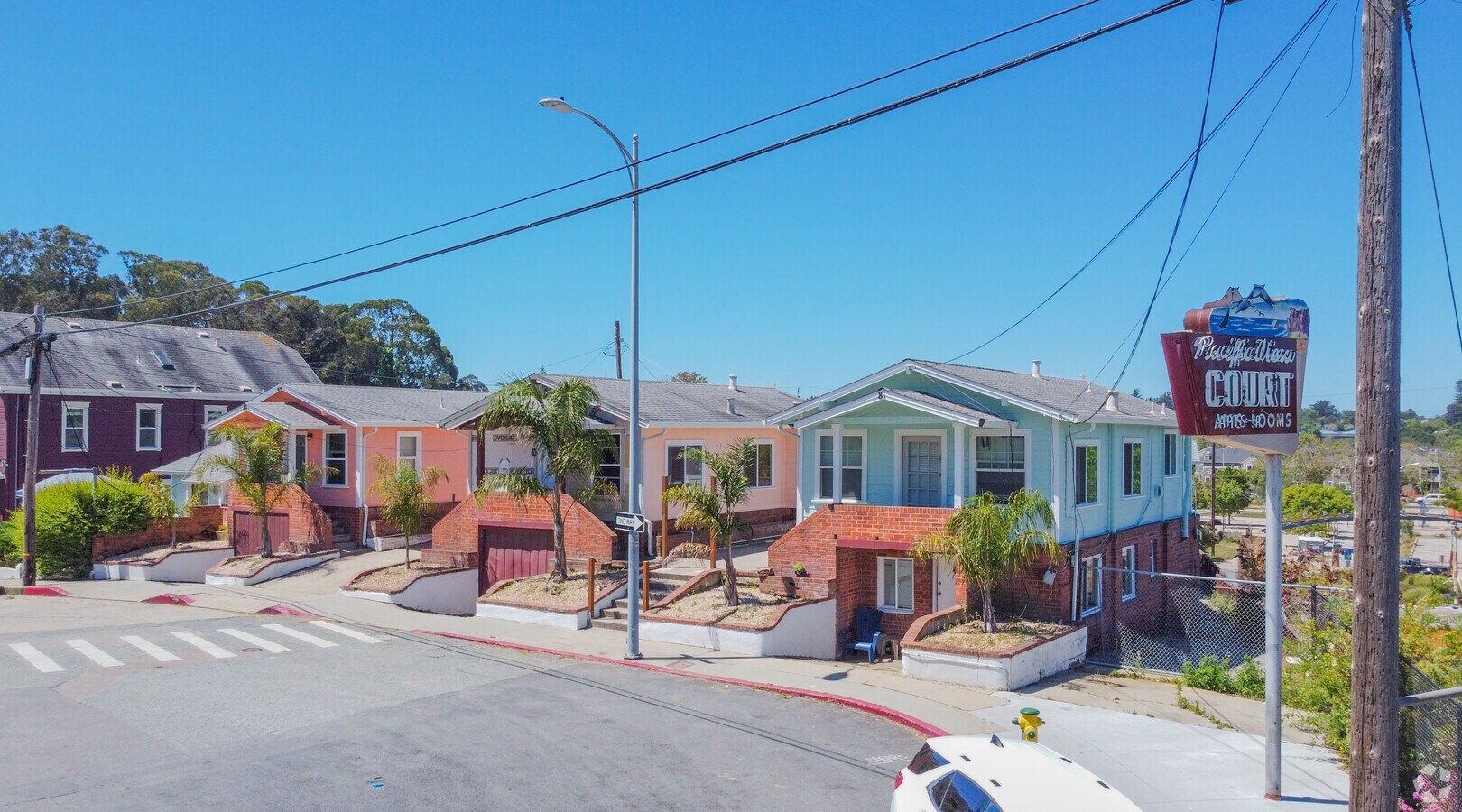 Houses in a row on a sunny day. Pink, mint green, and gray buildings with a street sign.