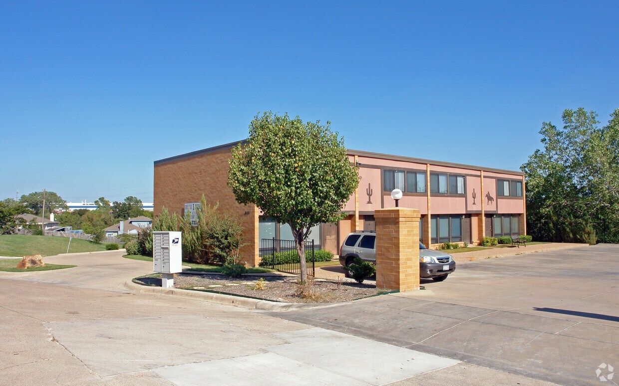 Two-story brick building with parking lot and a tree in front. Bright sunny day.