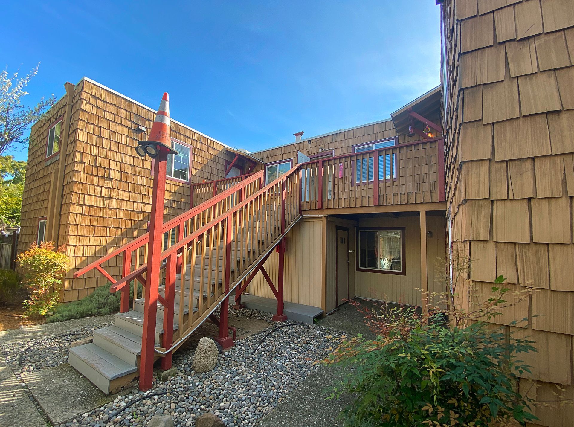Two-story building with wooden shingle siding and a red stairway. Blue sky overhead.