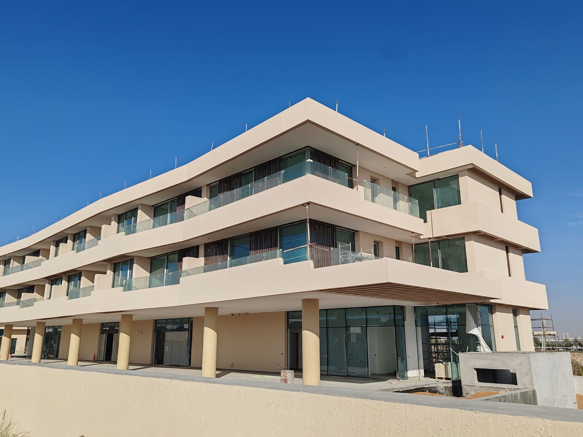 Beige multi-story building under construction against a clear blue sky.