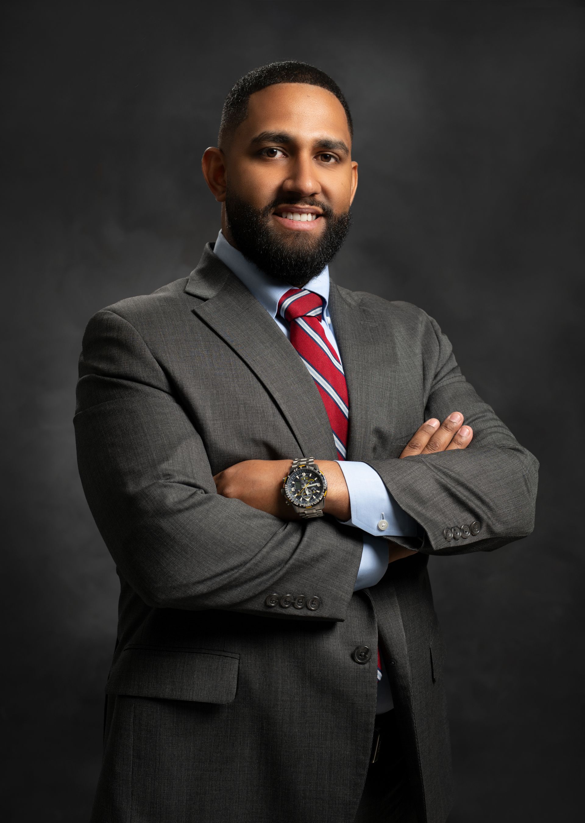 Man in gray suit and blue shirt smiles, headshot against a gray backdrop.