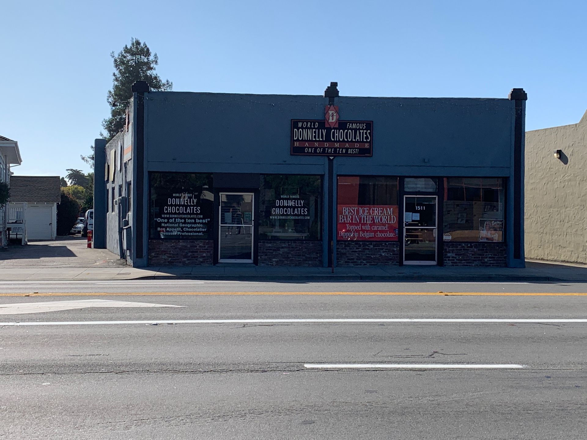 A blue storefront with two entrances and signage, facing a street under a clear sky.