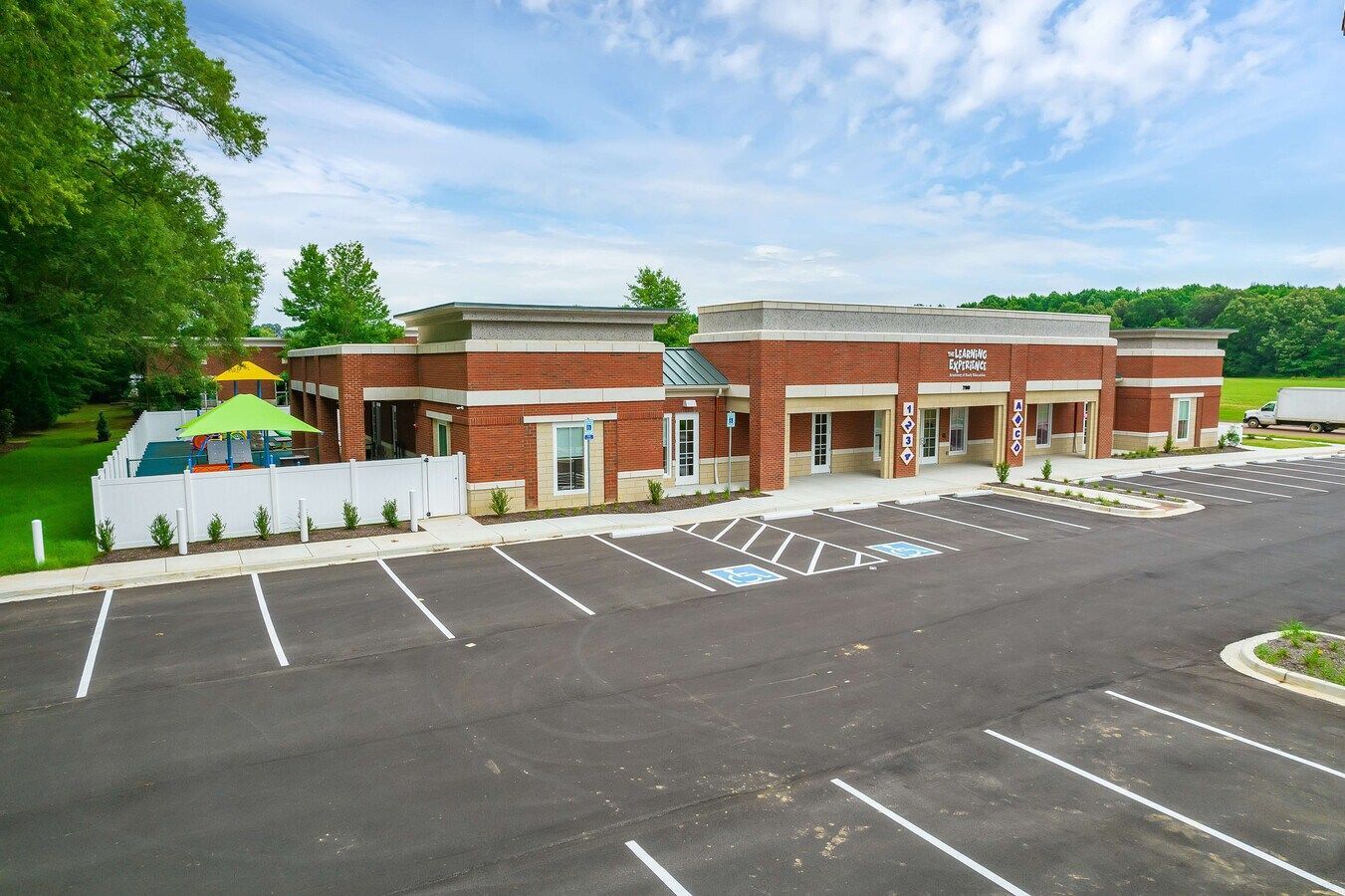 Brick building with parking lot and outdoor seating area under a blue sky.