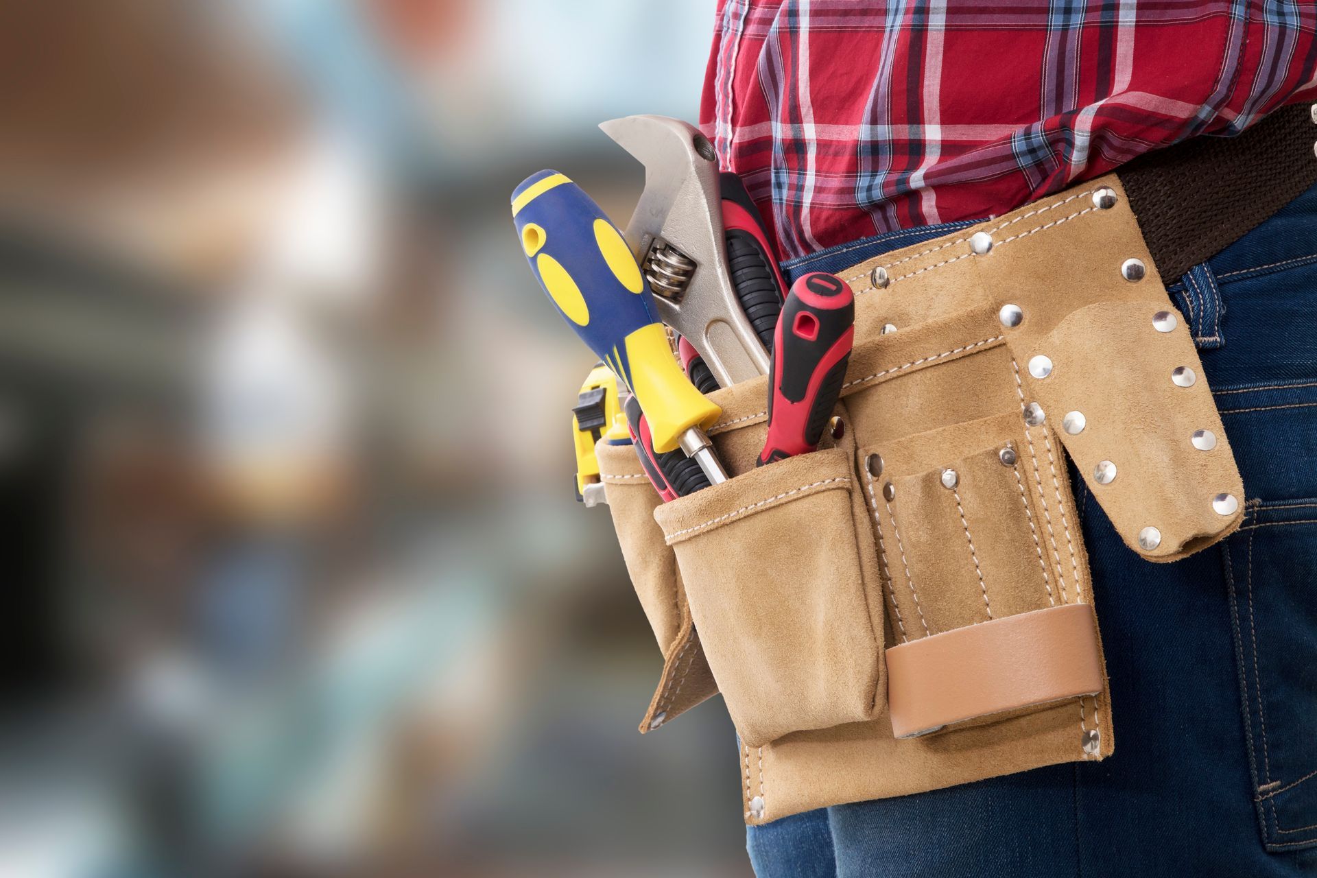 Tool belt with tools on a person wearing a plaid shirt and jeans.