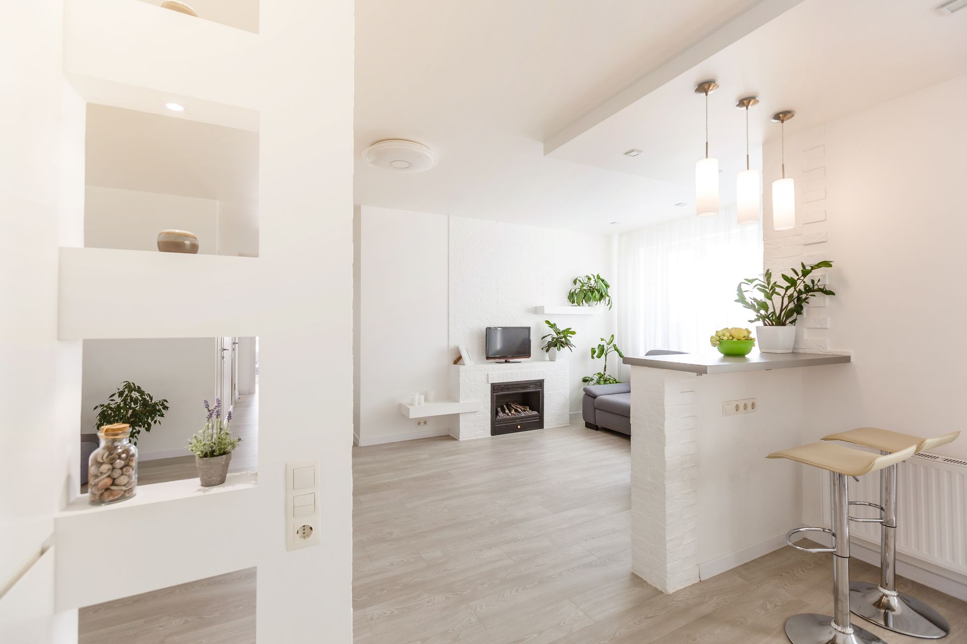 Modern, bright white interior with a bar area, small fireplace, and decorative shelving; plants and minimalist decor.