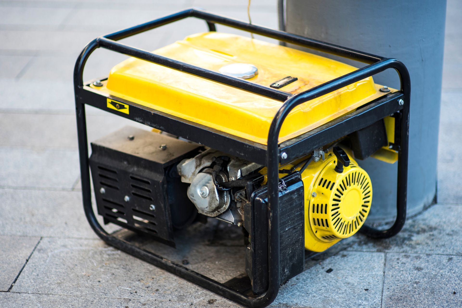 a yellow portable generator is sitting on the sidewalk next to a trash can .