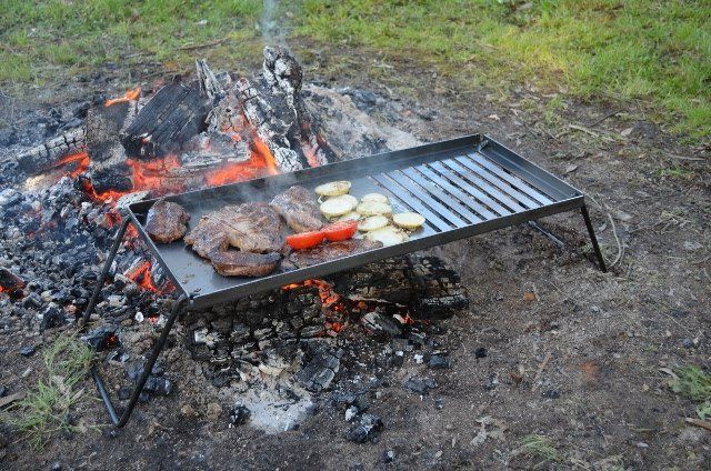 A grill with meat and vegetables on it is cooking over a fire.