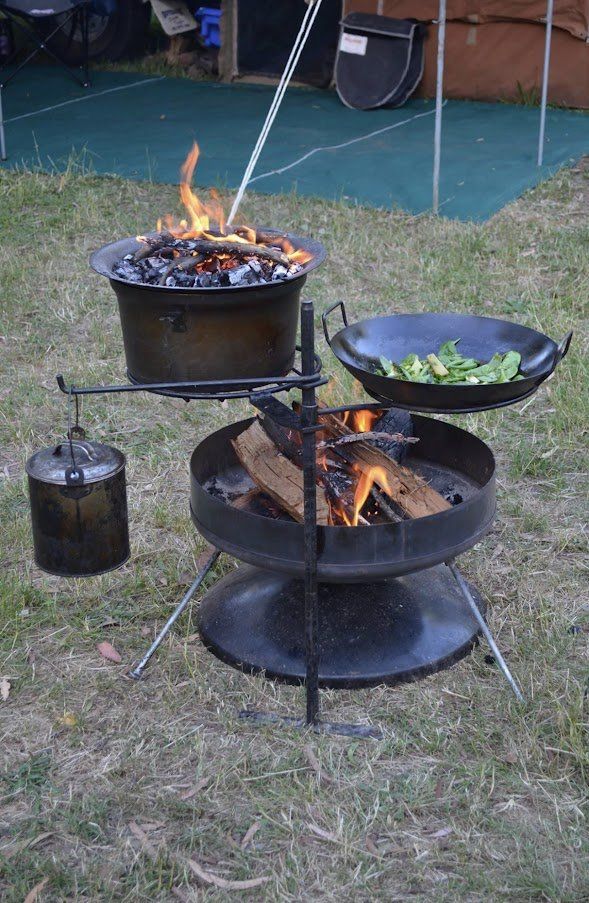 A fire pit with pots and pans cooking over it.