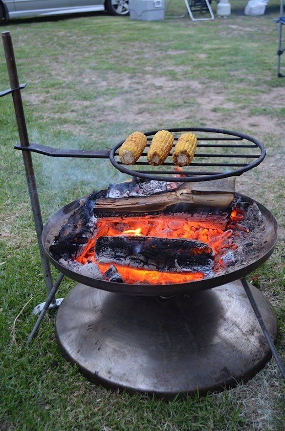 Corn on the cob is being cooked on a grill over a fire pit.