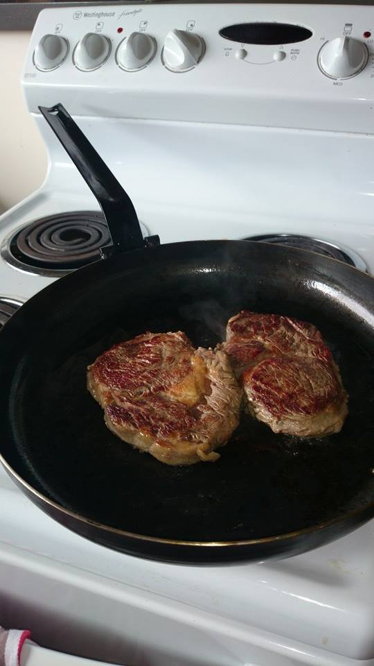 Two steaks are cooking in a frying pan on a stove