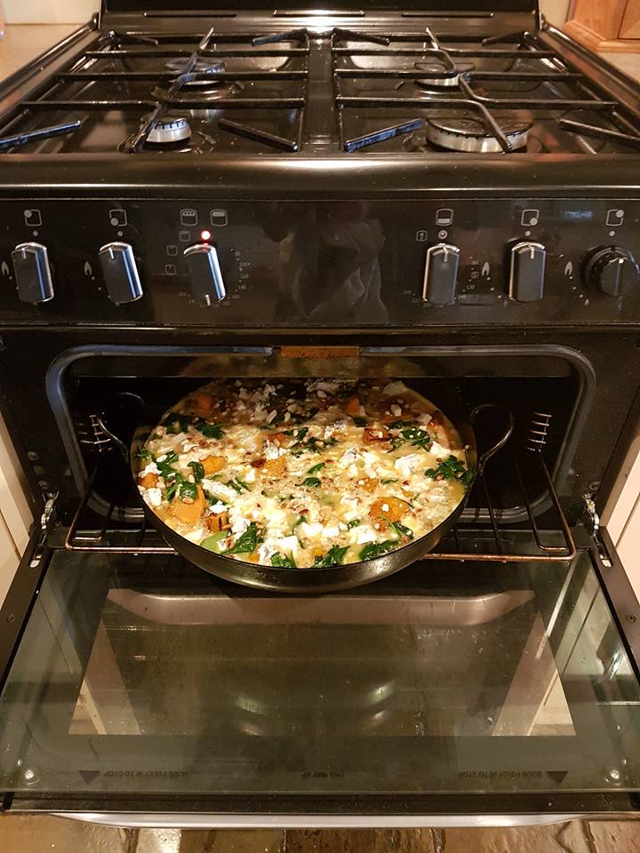 A pizza is cooking on a stove with the door open.