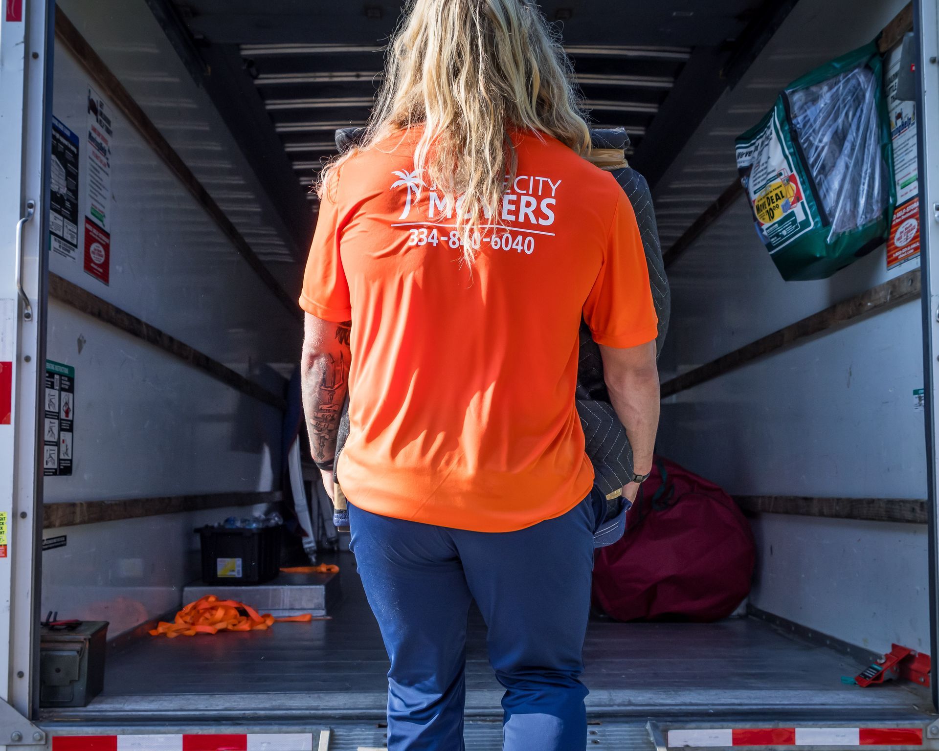 A woman in an orange shirt is walking into a moving truck.