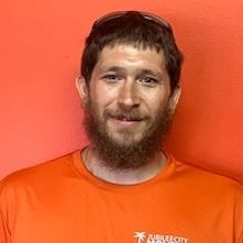 A man with a beard and sunglasses is wearing an orange shirt.