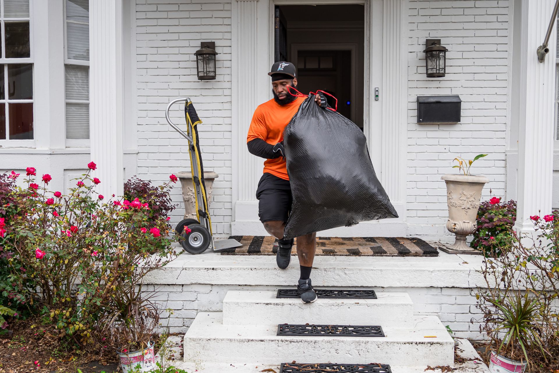 A man is carrying a large black bag of trash into a house.