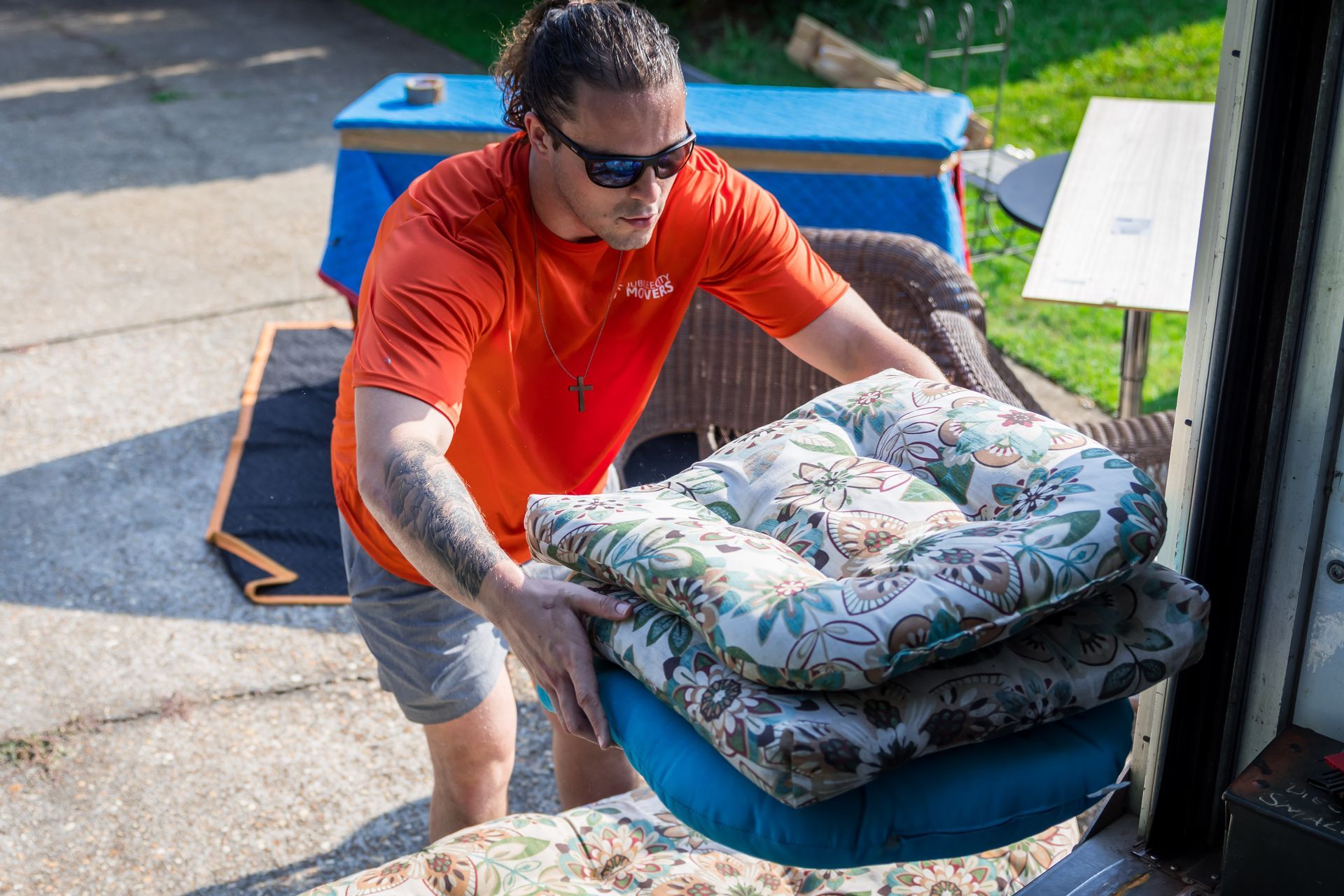 A man is carrying a stack of cushions out of a truck.