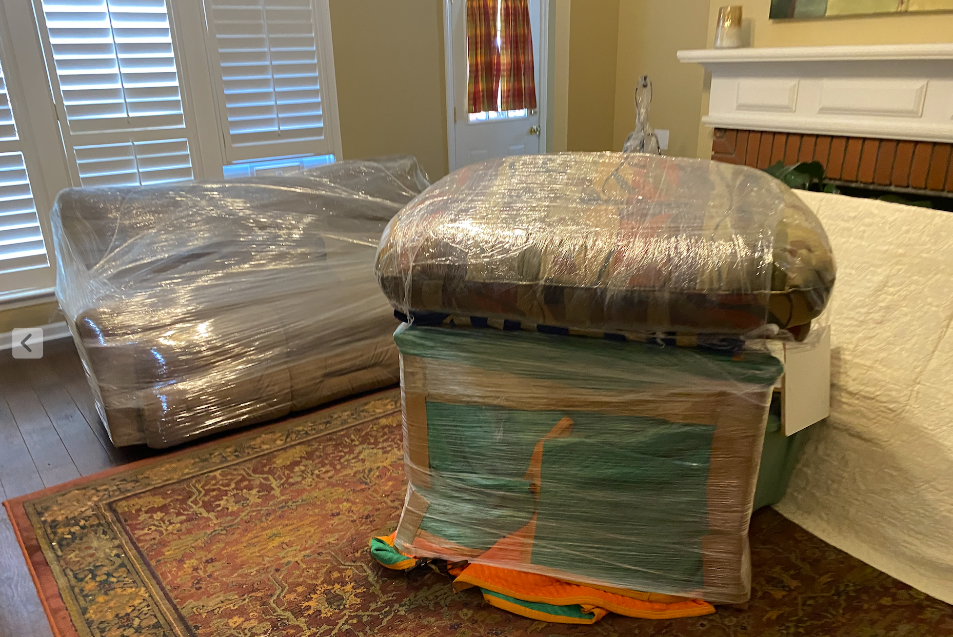 A couch and ottoman are wrapped in plastic wrap in a living room.