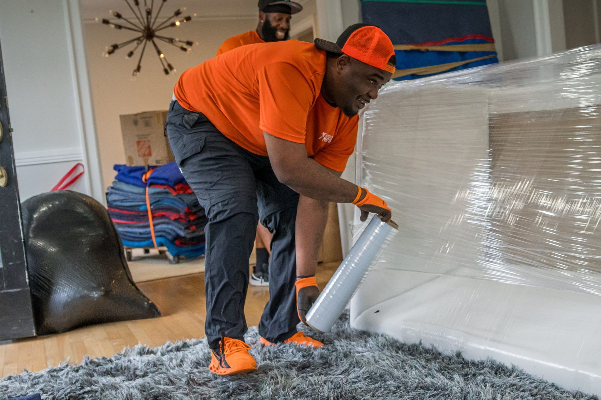 A man is wrapping a rug with plastic wrap in a living room.