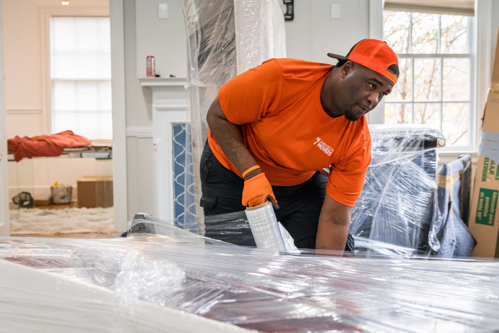 A man is wrapping a couch in plastic wrap in a living room.