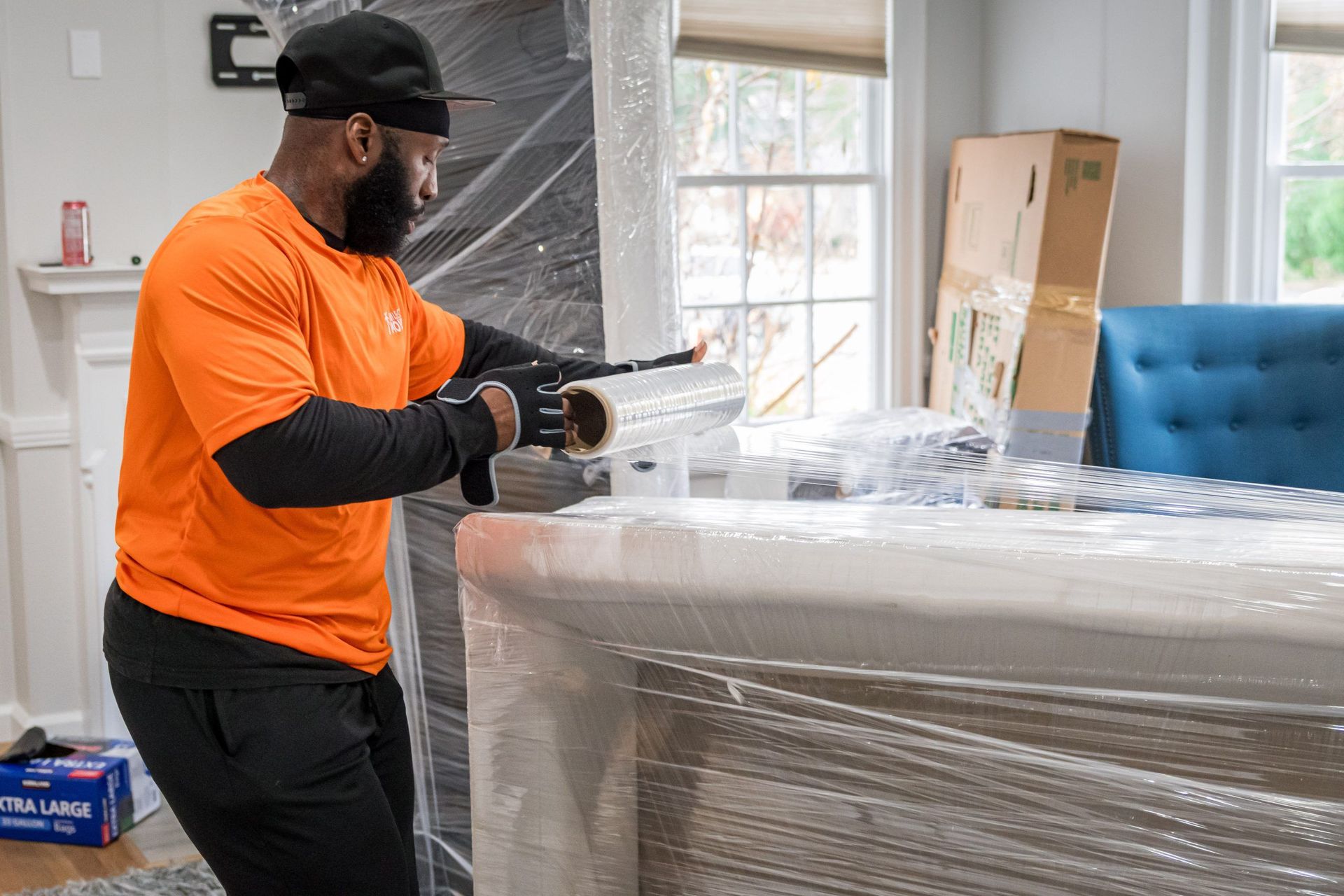 A man is wrapping a table with plastic wrap in a living room.