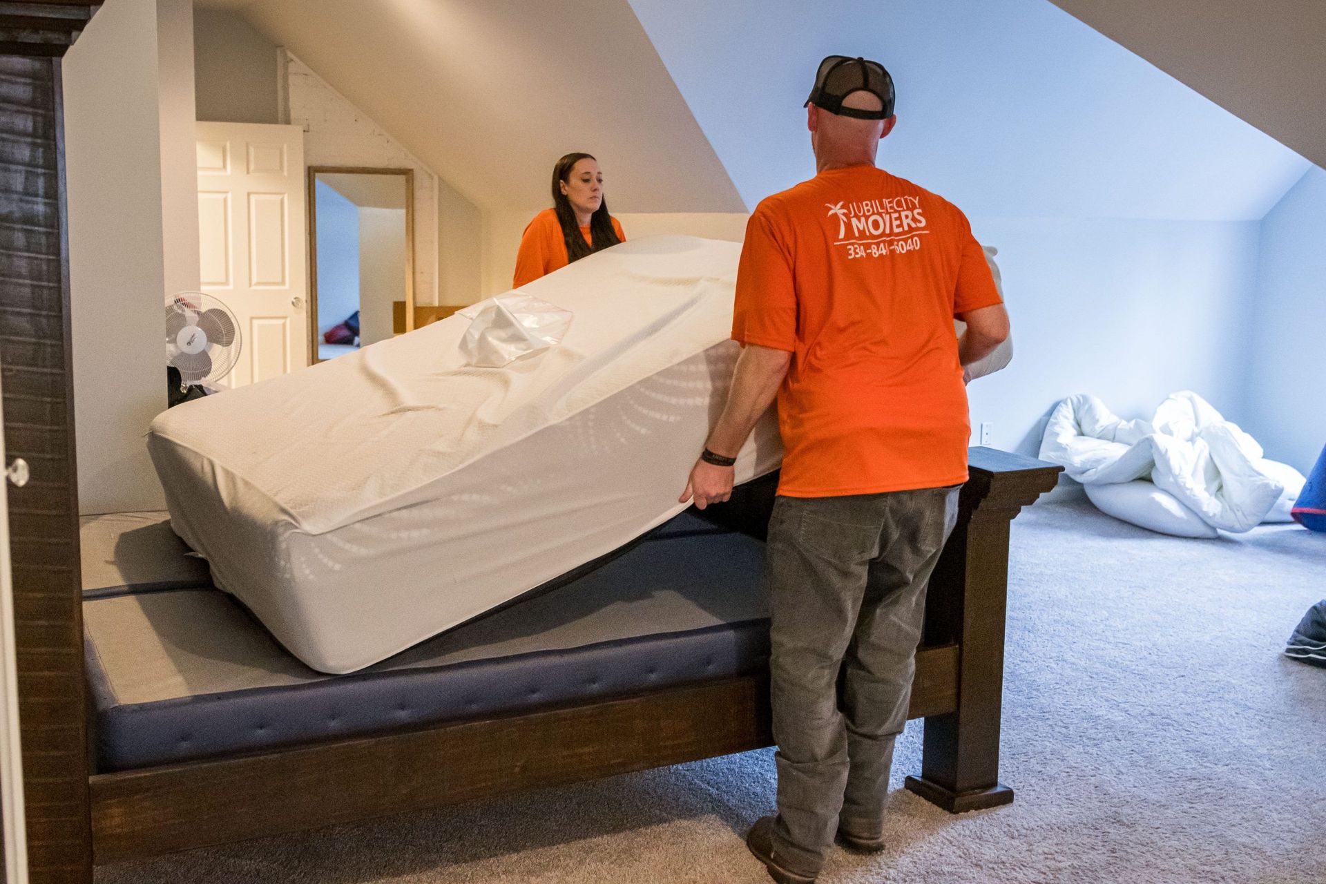 A man and a woman are moving a mattress into a bedroom.