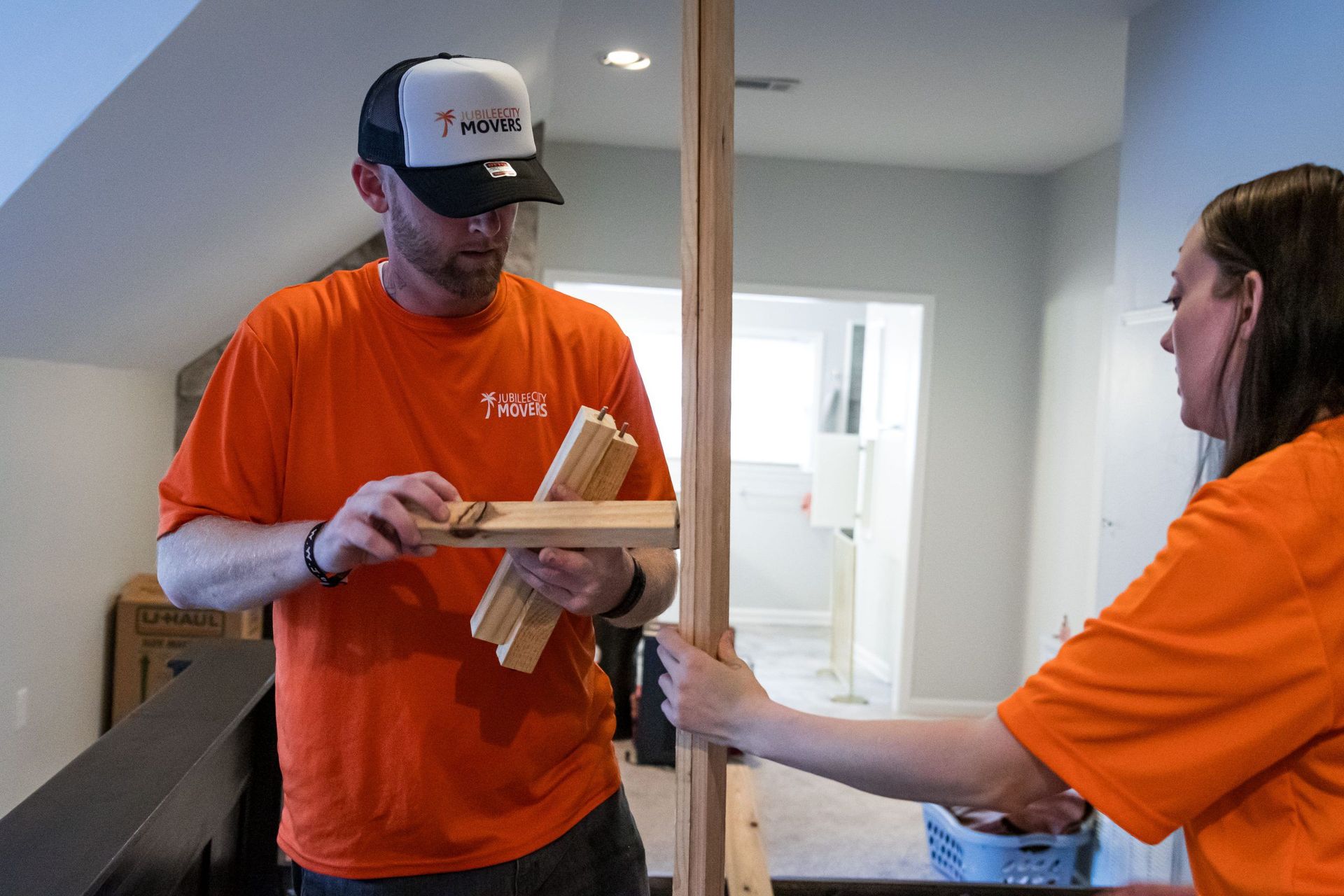 A man in an orange shirt is holding a piece of wood next to a woman in an orange shirt.