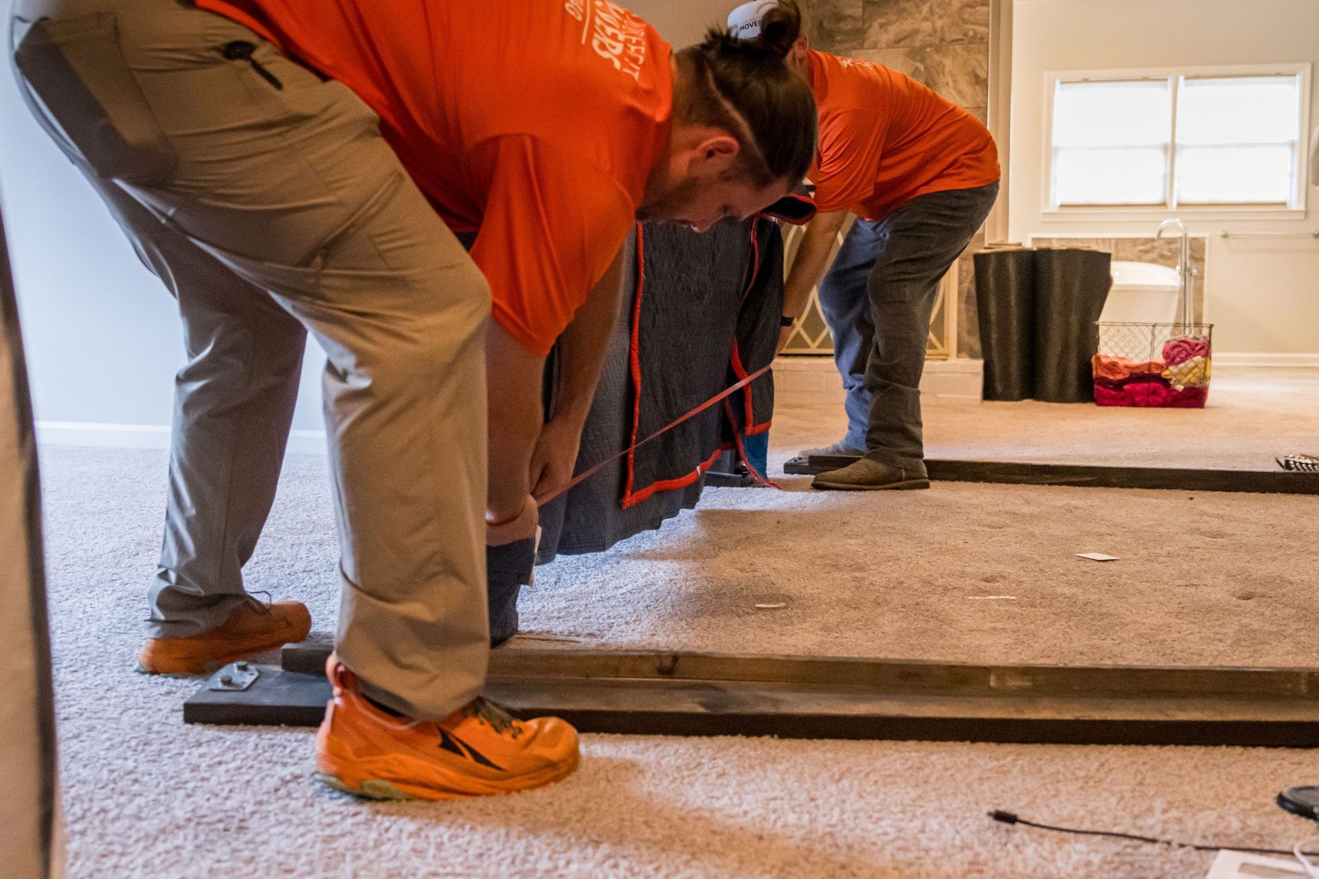 A man and a woman are moving a couch in a living room.
