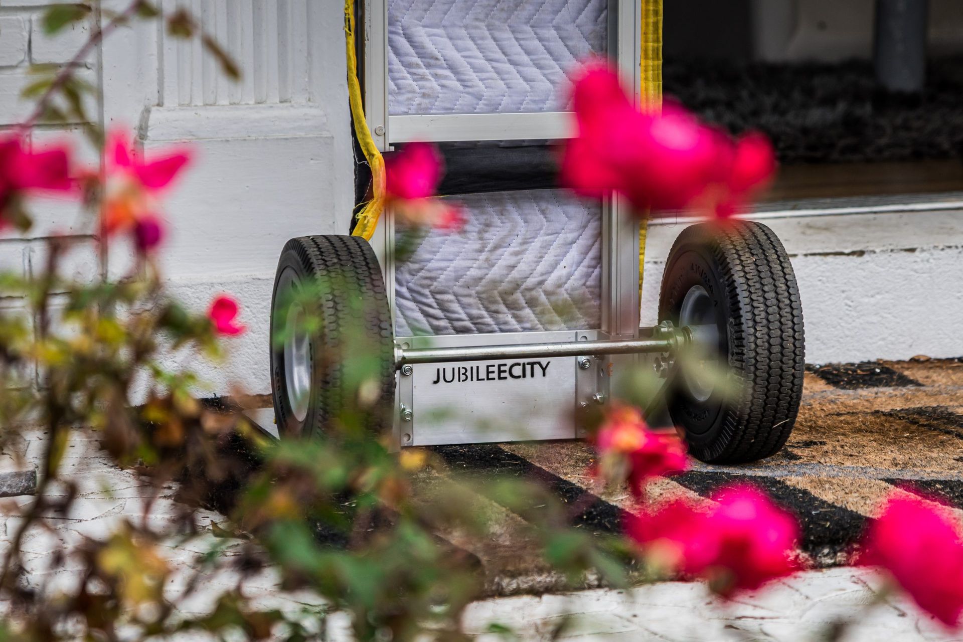 A moving cart is parked in front of a house with pink flowers in the foreground.