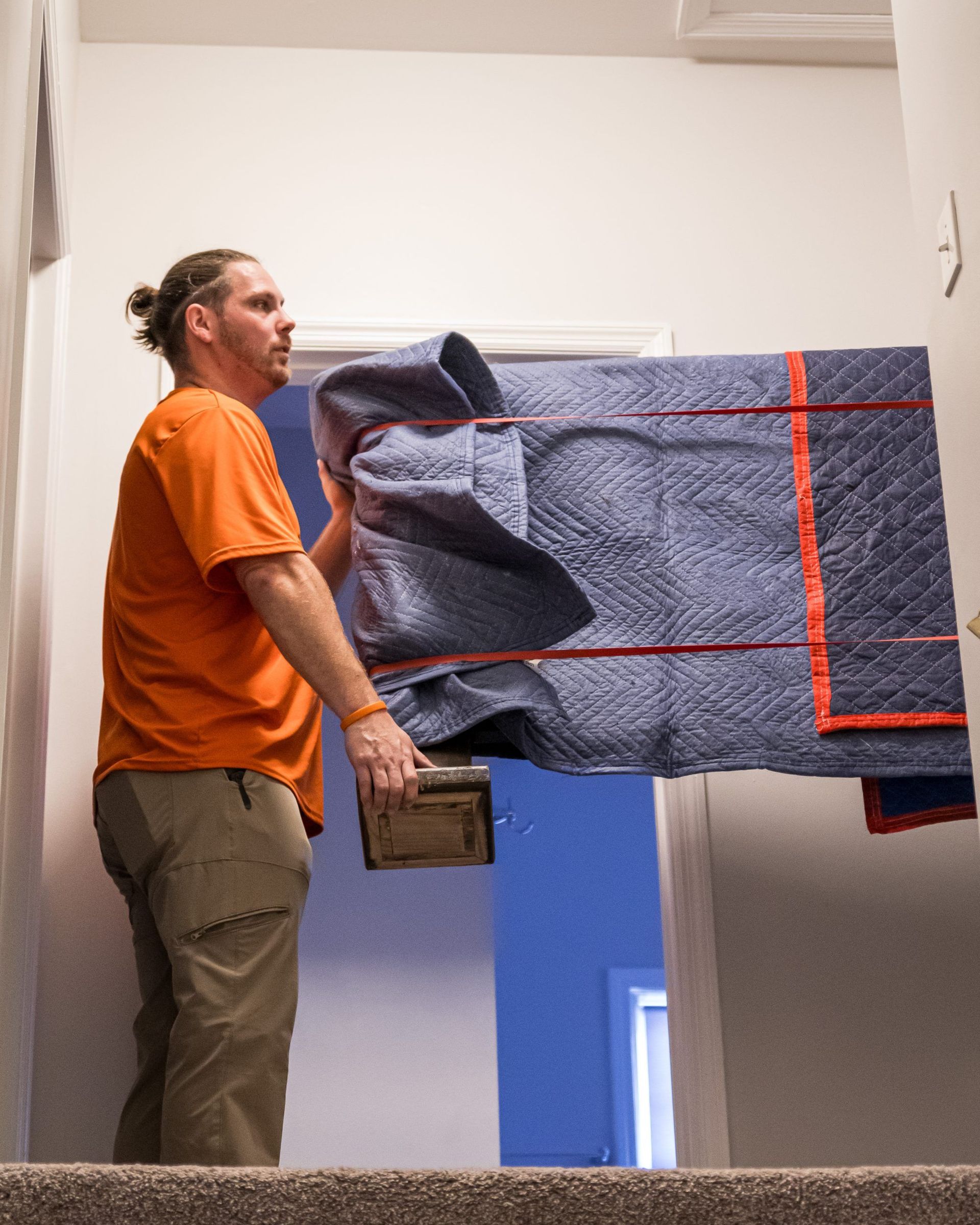 A man in an orange shirt is carrying a large piece of furniture