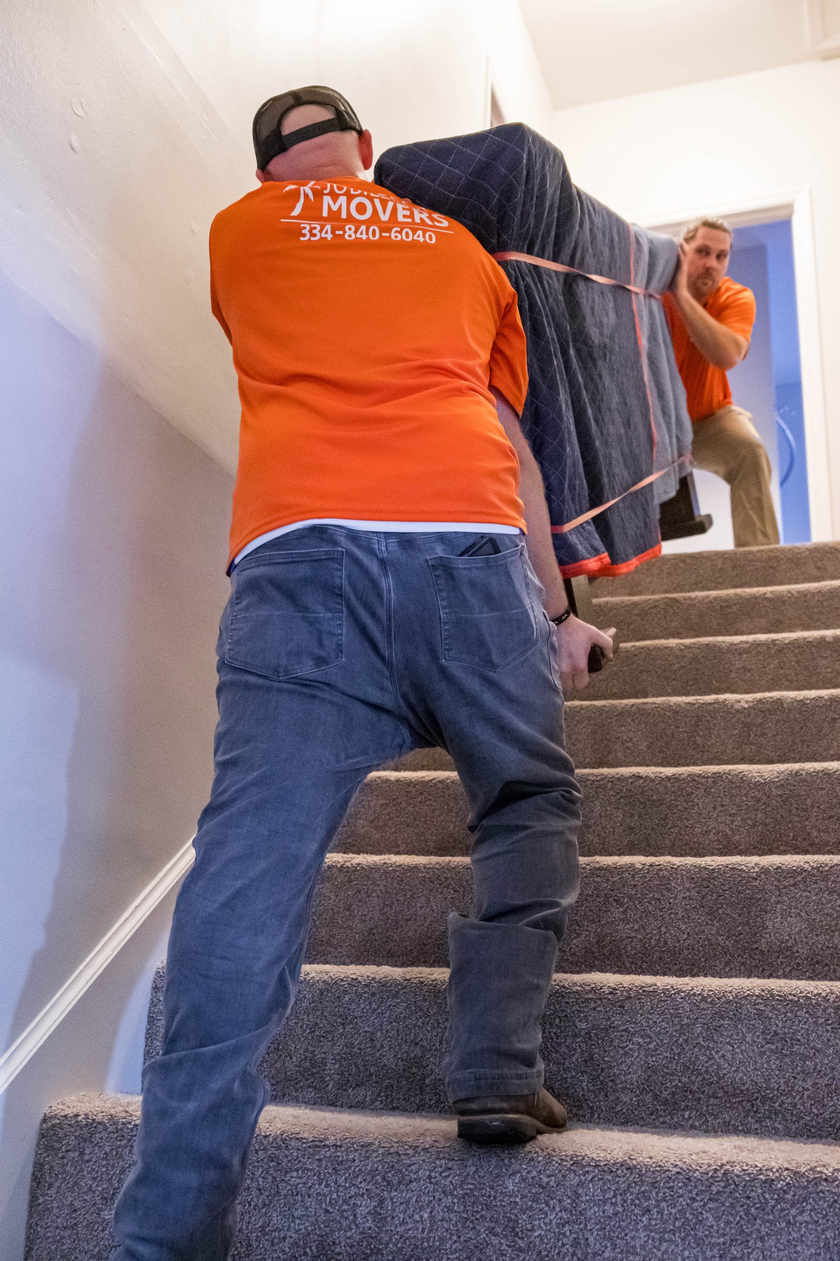 Two men are carrying a large piece of furniture up a set of stairs.