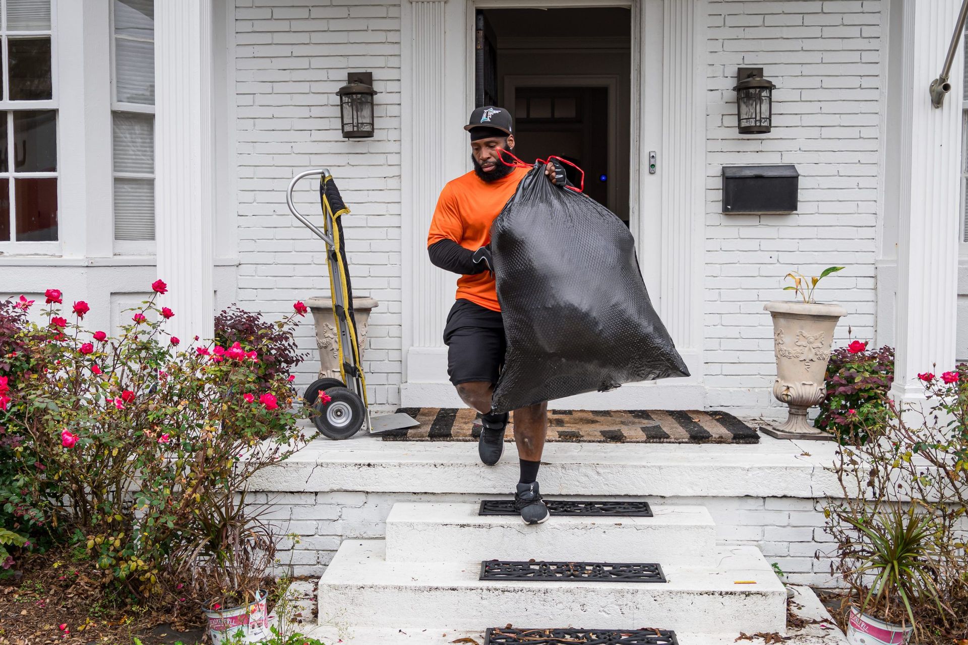 A man is carrying a large black bag in front of a white house.