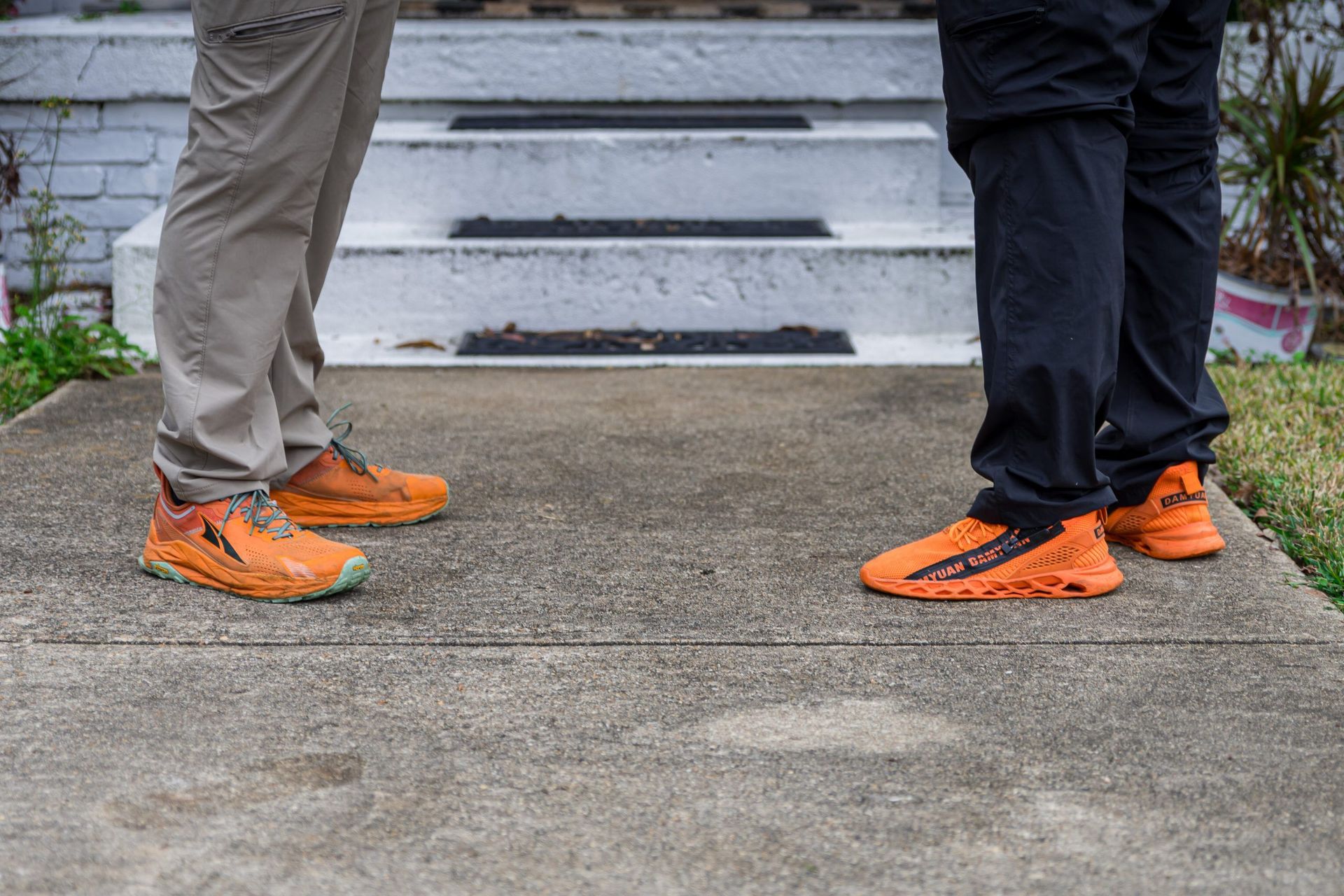 Two people wearing orange shoes are standing next to each other on a sidewalk.