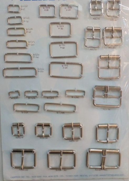 Hebillas de cinturón y herrajes metálicos surtidos dispuestos en filas sobre un fondo claro.