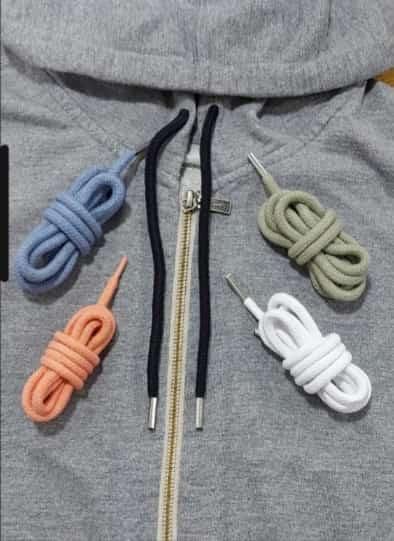 Cuatro tiradores de cremallera en espiral de color azul, coral, verde oliva y blanco sobre una sudadera con capucha gris.