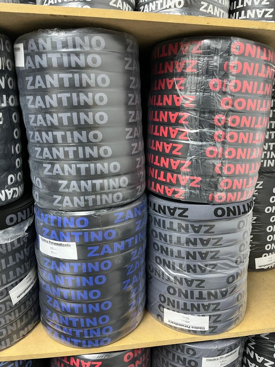 Rollos de papel higiénico de la marca Zantino apilados en negro, gris, rojo y azul en los estantes de las tiendas.