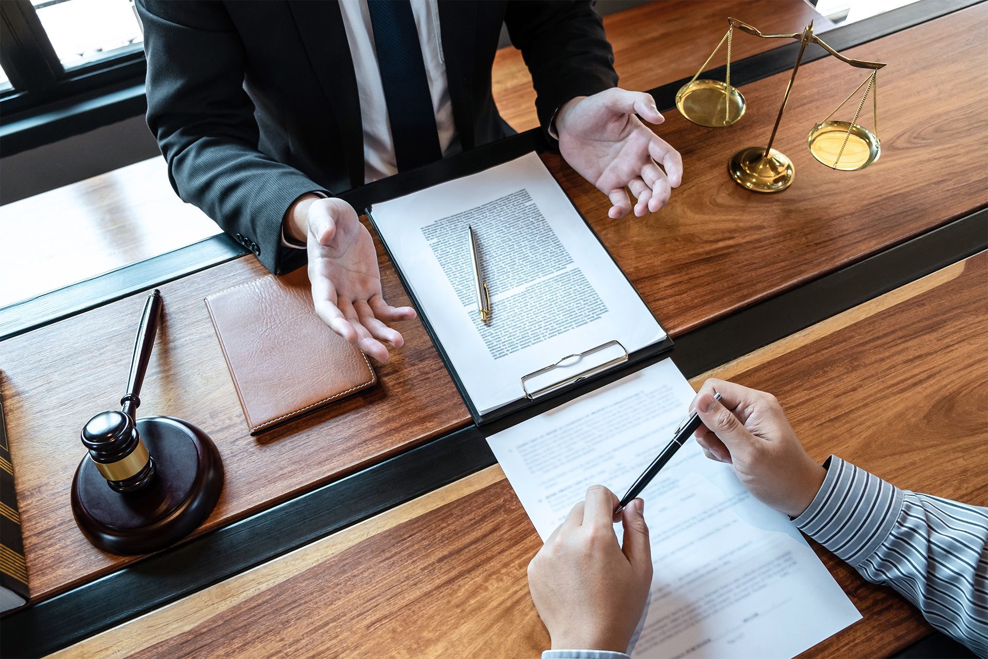 Lawyer explaining documents to a client, scales of justice and gavel on the desk.