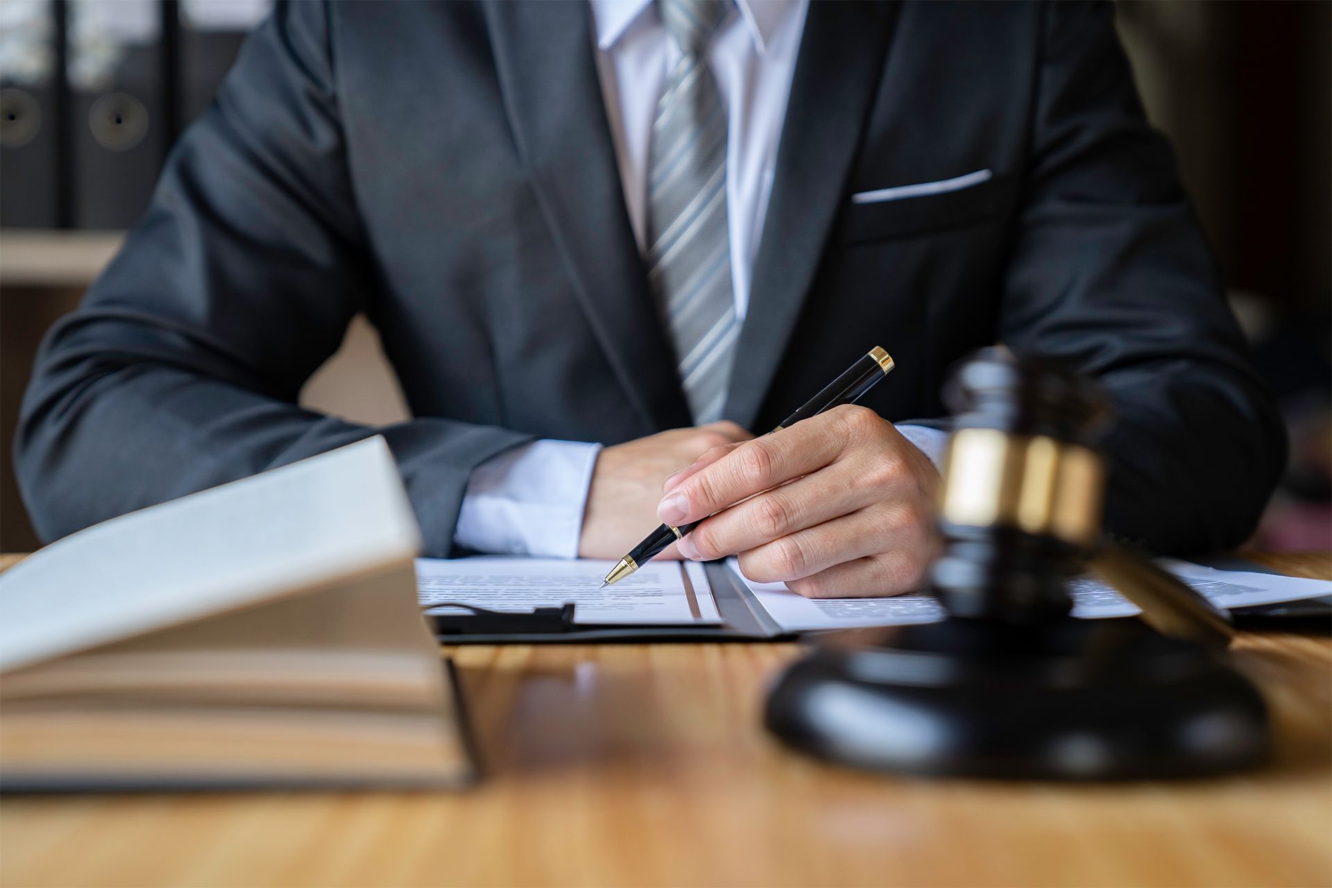 Lawyer in suit writing on documents with a gavel on desk.