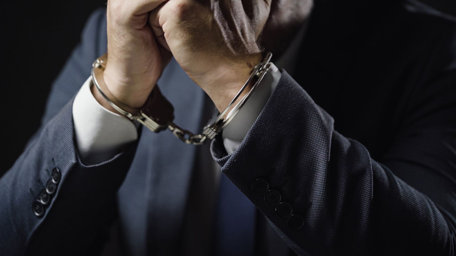 Man in suit with hands clasped in handcuffs