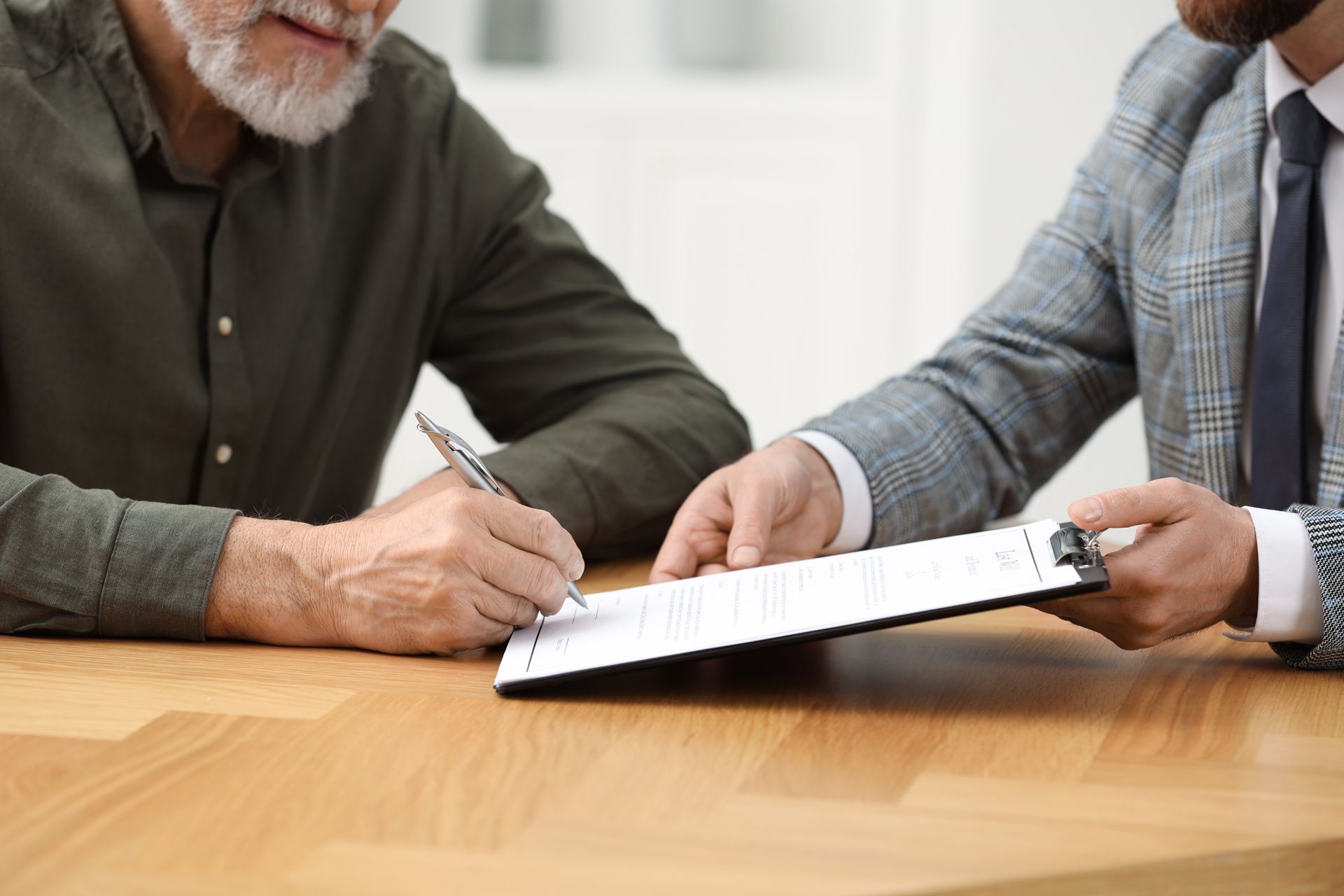 Older man signing document while being assisted by another man at a table