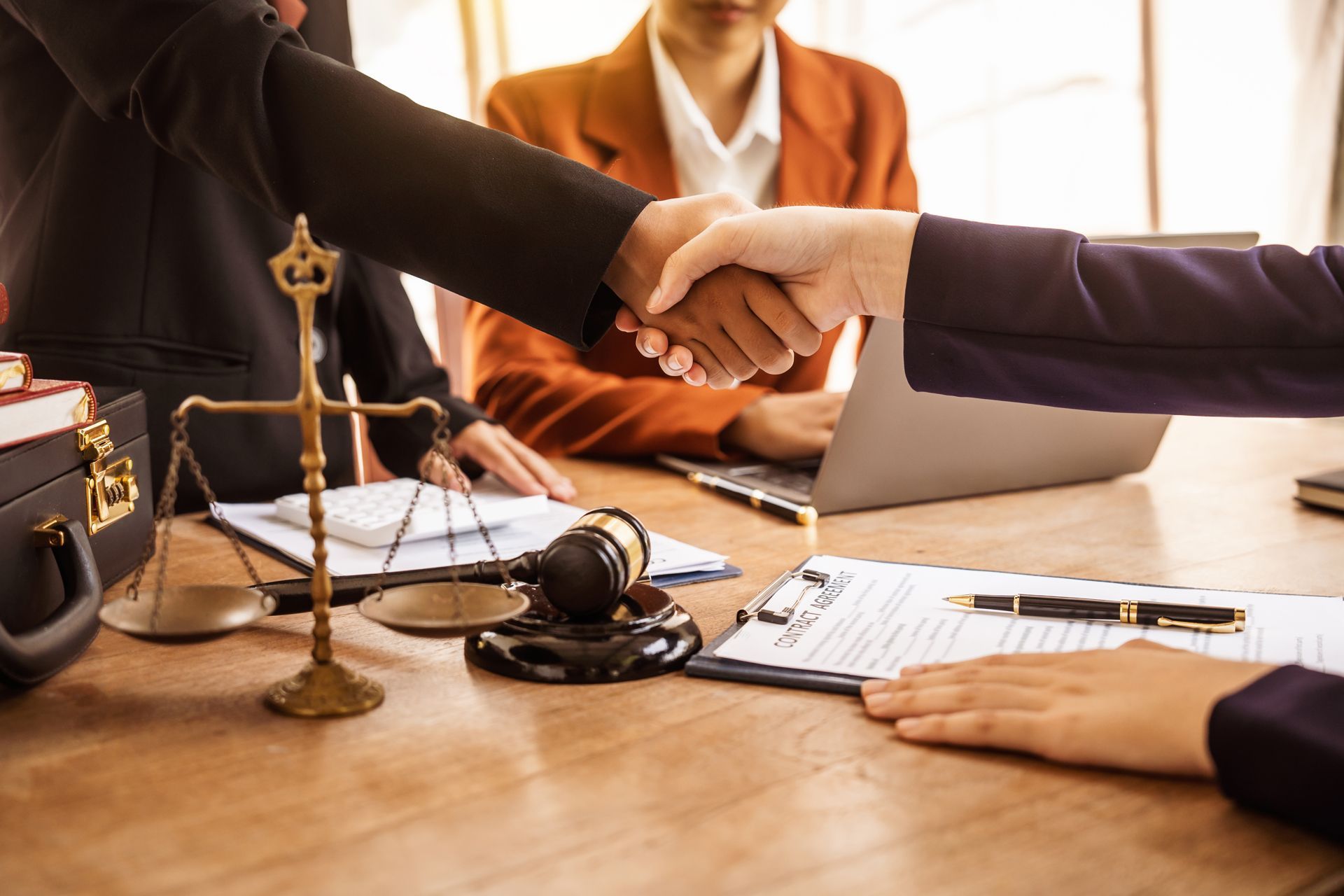 People shaking hands in a law office, documents, gavel, and scales on a table