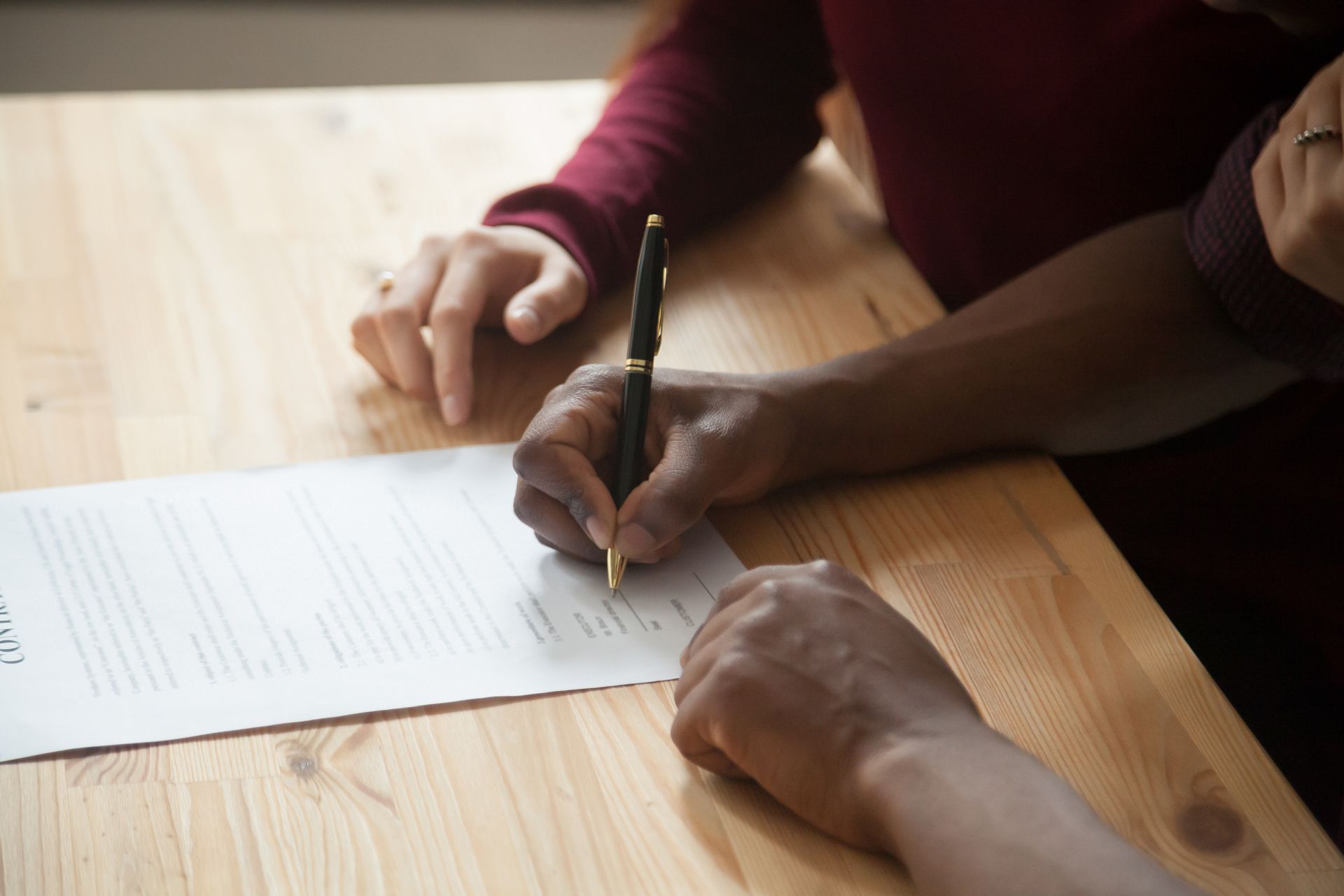 Person signing a document with a pen on a wooden table