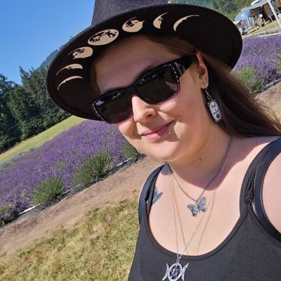 Woman in a witch hat and sunglasses smiles at a lavender field.