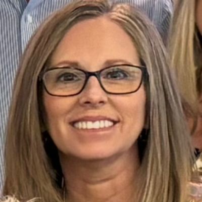 Woman with glasses smiling, medium-length blonde hair, close-up shot.