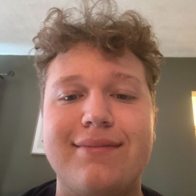 Close-up of a person with curly light brown hair smiling at the camera indoors.