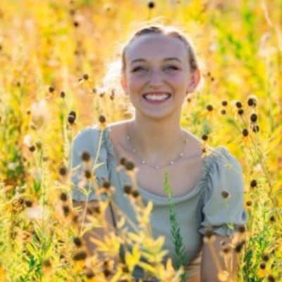 Woman smiling in a field of yellow flowers, wearing a light blue shirt.