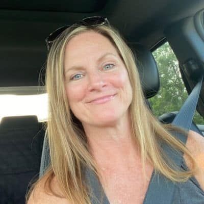 Woman with blonde hair smiling in a car, wearing sunglasses on her head.