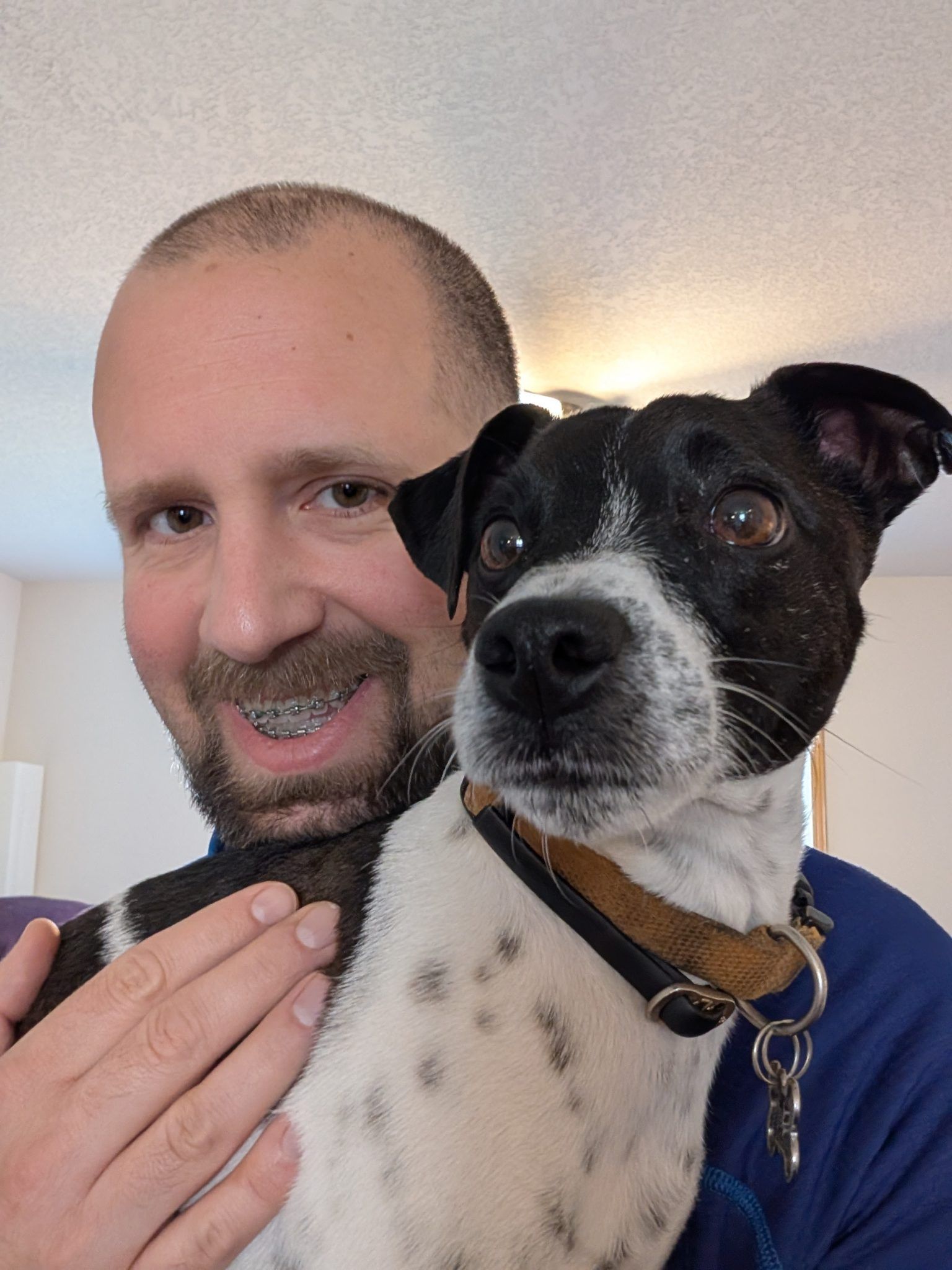 Man with braces holding a black and white spotted dog, smiling.