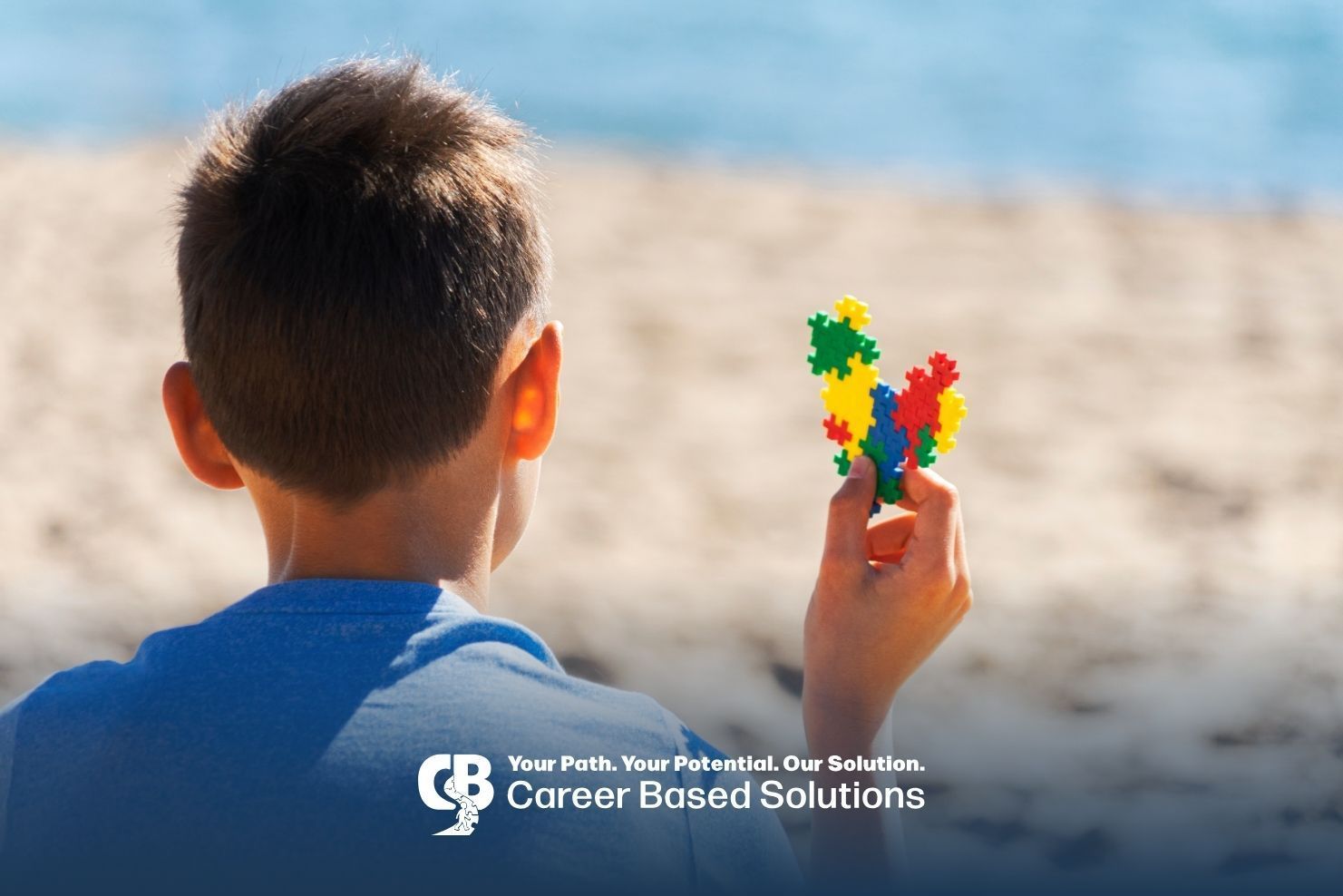 Autistic boy holds a colorful puzzle while looking toward the beach, encouraging calm sensory play