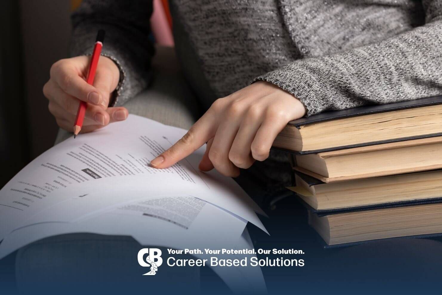 A therapist is sitting on a couch, holding a pencil and pointing to a document, with several books.