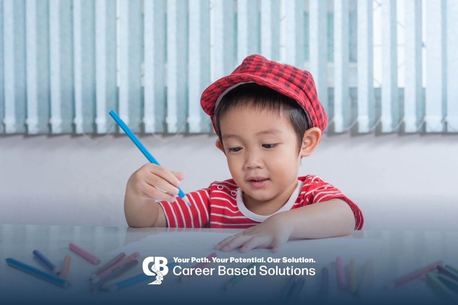 Autistic boy wearing a red cap drawing with colored pencils at a table, practicing creativity.