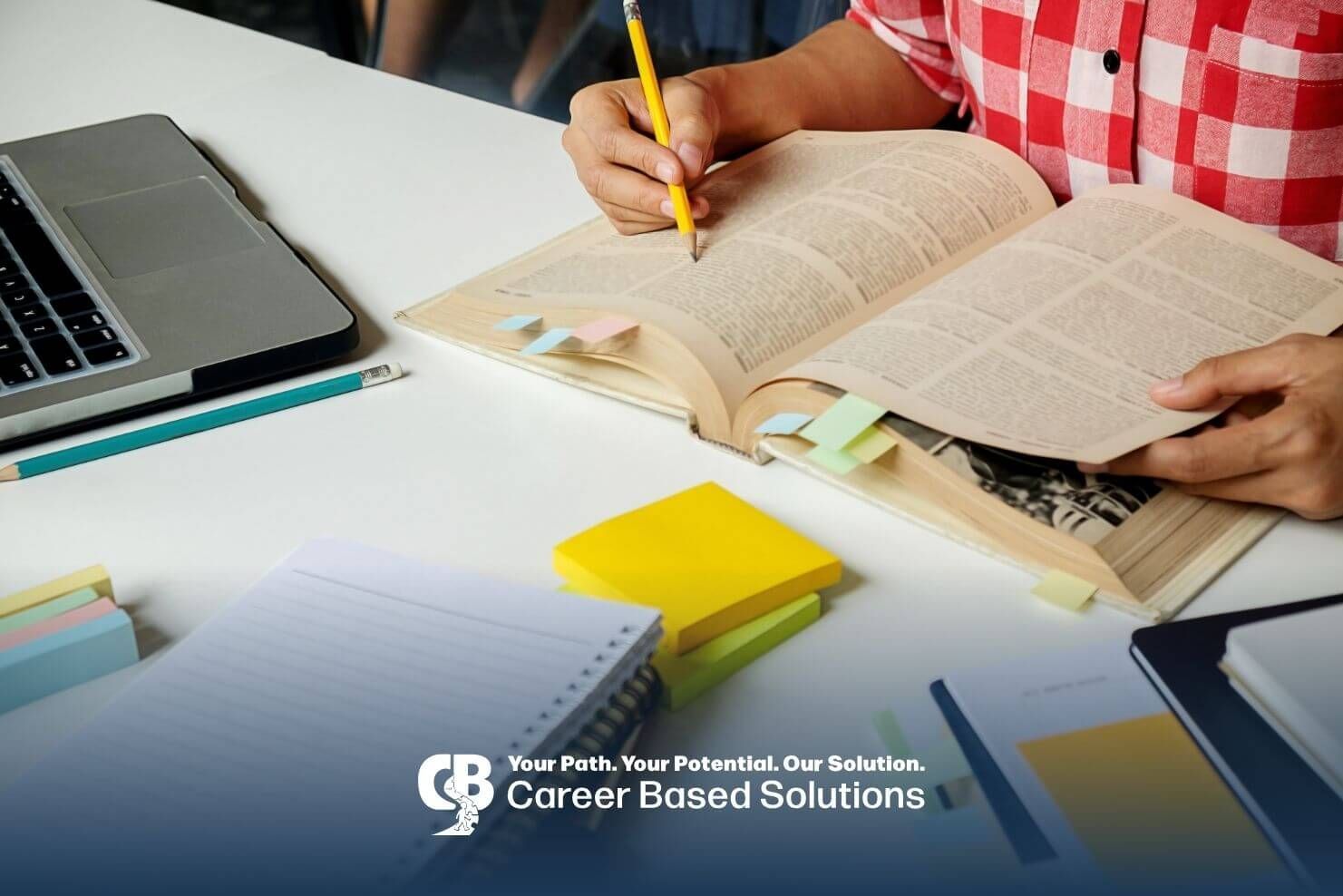 A person sitting at a table is writing on a page of a dictionary, surrounded by sticky notes.